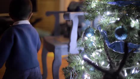 hermoso niño latino caminando hacia el árbol de navidad para colocar una burbuja azul