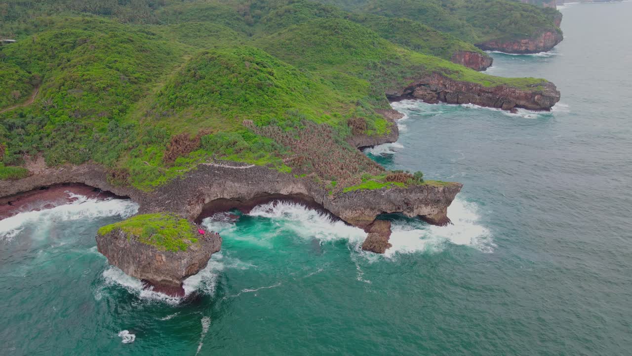 imágenes aéreas de una gran ola marina golpea la costa de coral en una isla cubierta de un denso bosque
