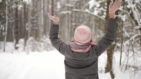 cámara lenta, una mujer con chaqueta, sombrero y bufanda en el invierno en el bosque sosteniendo nieve en sus manos y soplando hacia la cámara arroja nieve.