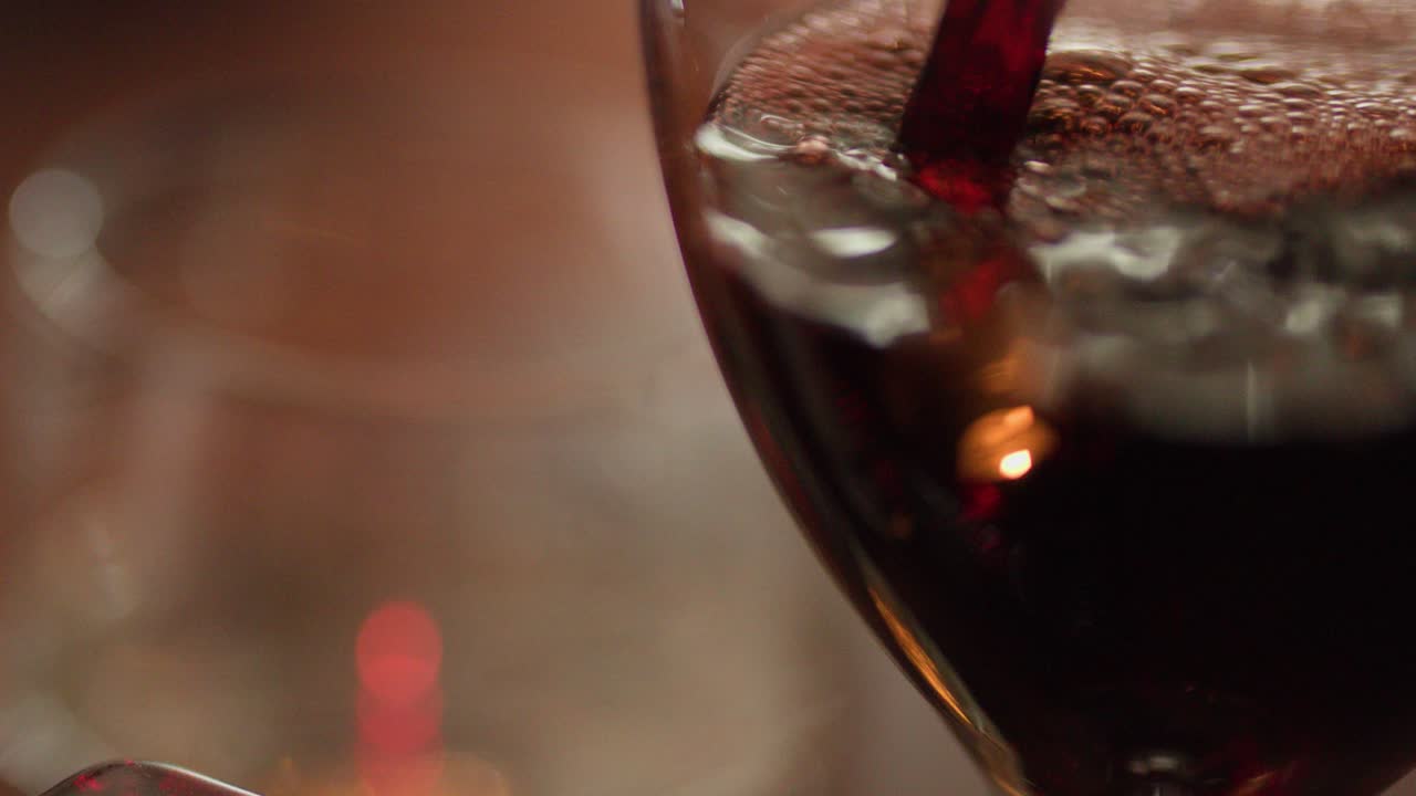 Primo piano di vino rosso versato in un bicchiere, luce calda di candela, messa a fuoco ridotta, atmosfera romantica da ristorante