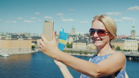 a happy tourist with the flag of sweden takes pictures of himself against the backdrop of stockholm'