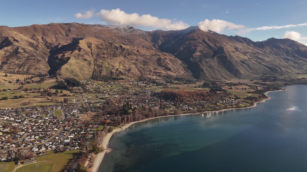 Dynamic 4K 60fps drone shot flying backwards along the Lake Wanaka shoreline. This cinematic reveal captures the town, the vast lake, and mountains. Ideal for travel or tourism projects