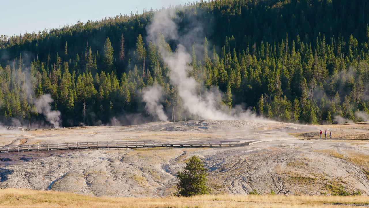 Steam rises from geothermal features in Yellowstone National Park with people on a boardwalk
