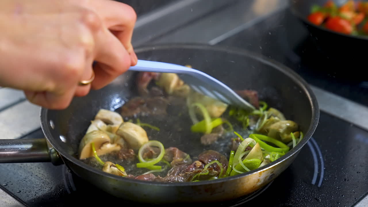 Mushrooms fried with vegetablesin a big frying pan. Chef turns fried ingredients with spatula.