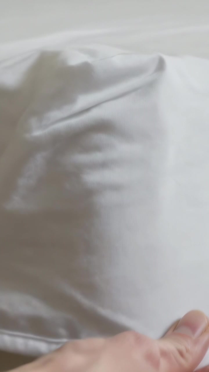 Video verticale: Una mano si allunga per rimboccare, tirare e lisciare una federa sul letto, rimuovendo le pieghe.