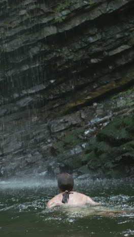 person swimming under a waterfall in a natural setting