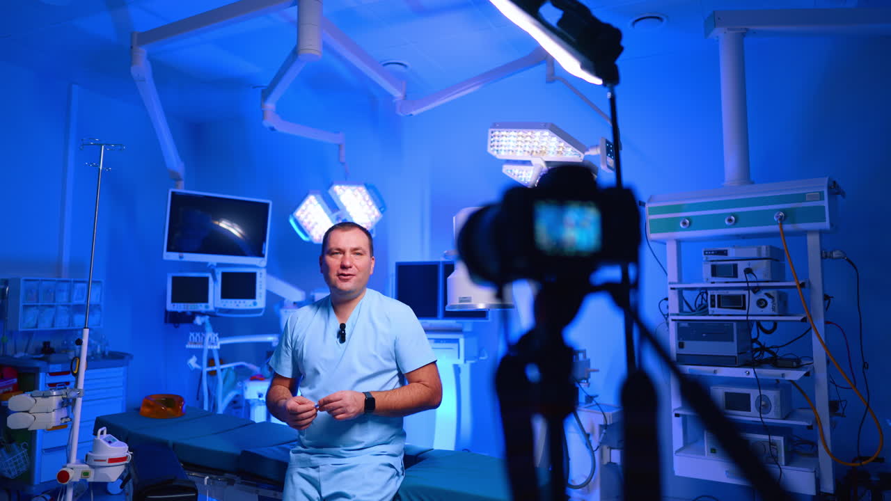Medico che filma un vlog medico in una sala operatoria blu. Il medico in camice si trova in sala operatoria, con la sagoma della telecamera in primo piano, illuminazione blu e attrezzatura chirurgica.
