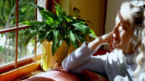 mature woman looking through window at home 4k