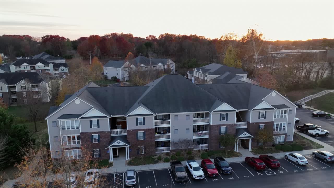 Several Modern apartment buildings or Multi-family units during sunset time with colored trees in fall. Suburb district with parking cars. Aerial wide shot