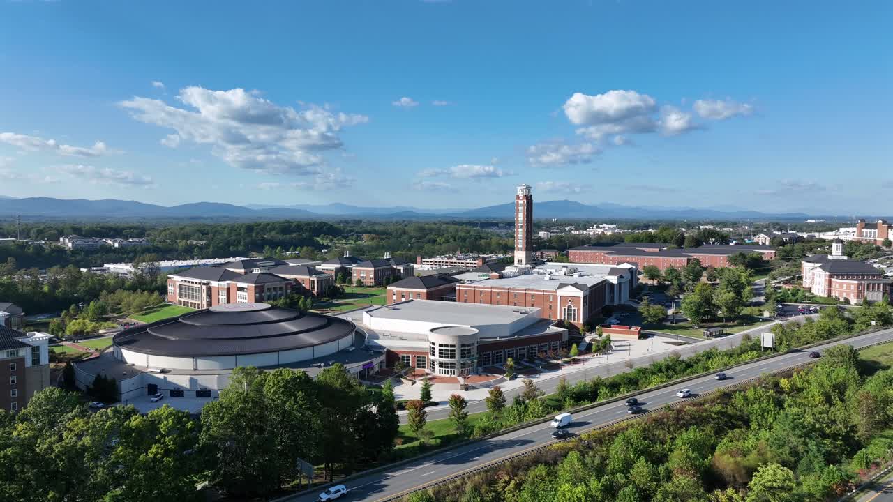 Traffic on interstate highway near historic liberty university in Virginia, USA. Aerial wide shot. Panorama view. Large campus with red brick buildings and houses. Mountains in distance. Sunny summer
