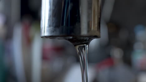 Close-up-of-a-slow-running-tap-against-a-blurred-background-in-kitchen-or-bathroom