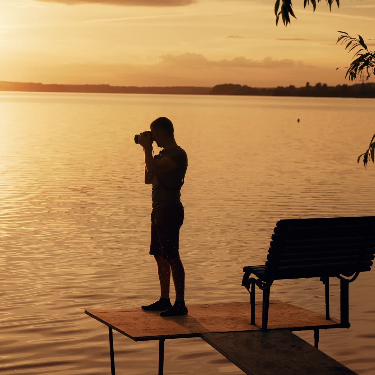 Man silhouette walking on the wooden pier on the river. Breathtaking golden sunset over the horizon.