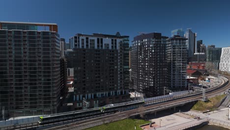 REM-automated-light-rail-system-subway-train-in-Montreal-city-with-skyline-building-in-Quebec,-Canada-aerial-drone-sunny-day