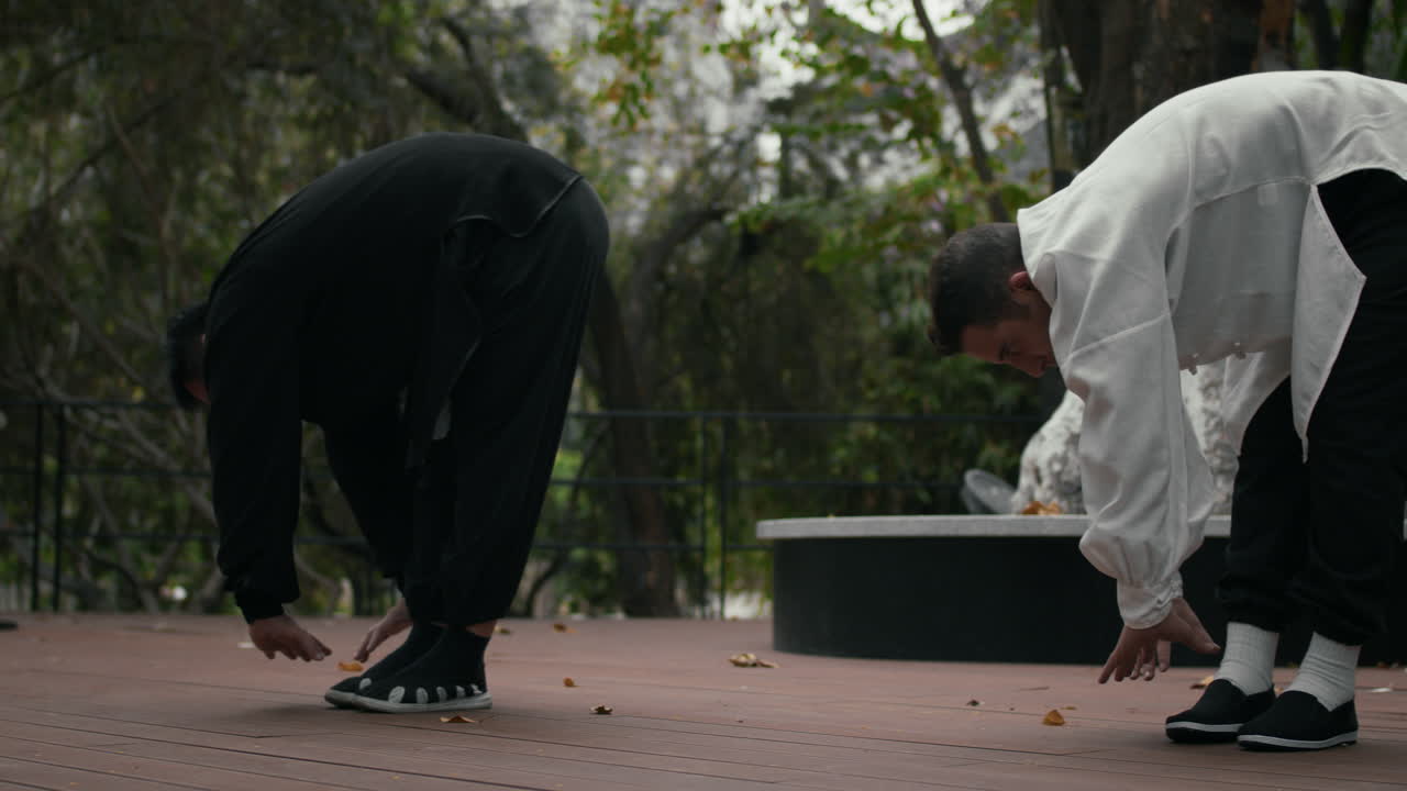 Two men practicing martial arts or Tai Chi warm-up stretches outdoors