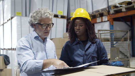 Focused-Caucasian-boss-and-female-African-American-worker-talking-in-warehouse