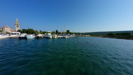 Cinematic-FPV-drone-flies-low-along-water-past-sailboats-docked-offshore-of-Osor-Croatia