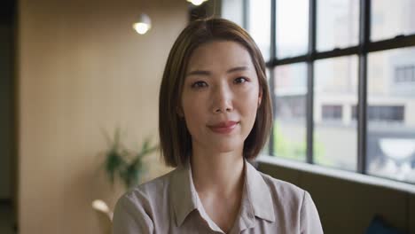 Asian-businesswoman-standing-looking-out-of-window-in-modern-office