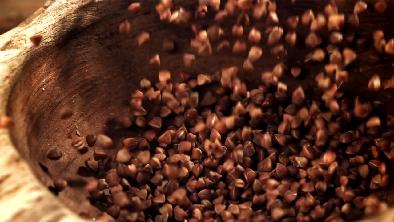 Chicchi di grano saraceno che cadono in una ciotola di legno rustica al rallentatore