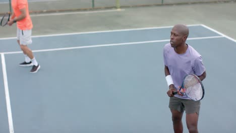 two diverse male friends playing doubles returning ball on outdoor court in slow motion