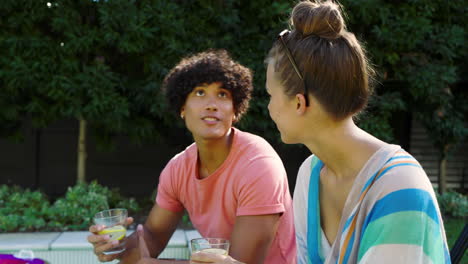 diverse couple enjoying refreshing drinks by poolside on sunny day, relaxing together