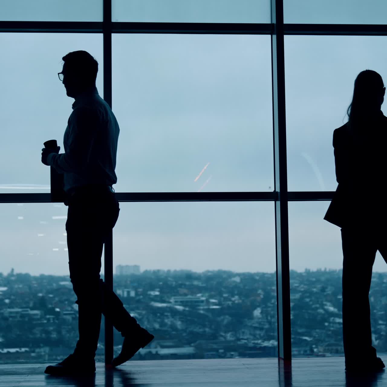 Sagome di dipendenti, uomo e donna, camminano vicino alla finestra. La donna parla al telefono e l'uomo beve caffè. Vista dal basso.