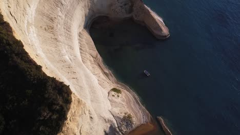 toma aérea de un pequeño bote flotante rodeado de enormes acantilados y mar en calma