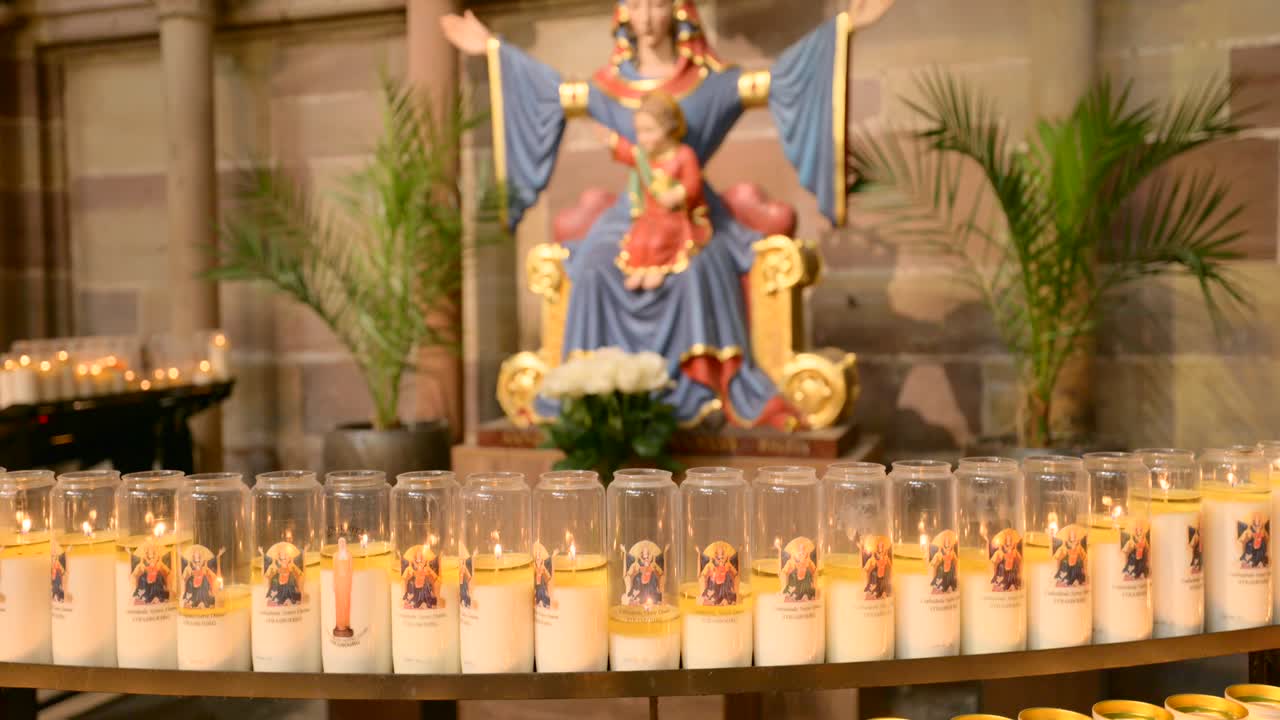 Una fila di candele votive arde di fronte a una statua religiosa all'interno della Cattedrale di Strasburgo. Ideale per concetti di fede, preghiera e devozione spirituale.