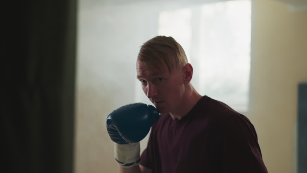 체육관에서 매달린 가방을 는 운동선수, 권투 장갑을 입은 프로 전투기, 스포츠 클럽에서 느린 동작으로 싱 가방을 가지고 훈련하는 운동선수