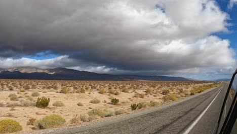 view of the mojave desert landscape with dark, ominous clouds overhead as seen from a vehicle driving through and looking back