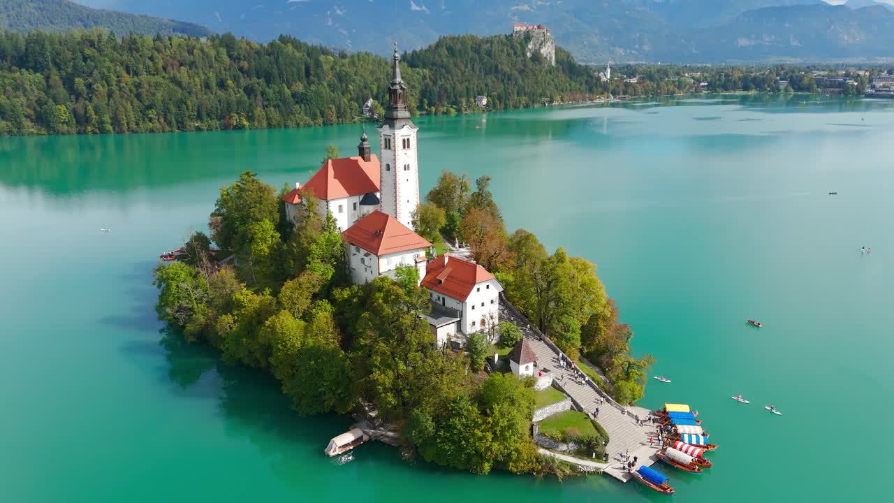 Giornata di sole a Isola di Bled e alla Chiesa dell'Assunzione di Santa Maria in Slovenia. Ampia ripresa aerea inclinata verso l'alto. Lago verde e barche