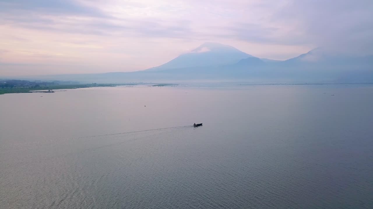 toma de un dron de un bote en medio de un enorme lago con una montaña al fondo - lago rawa pening, indonesia