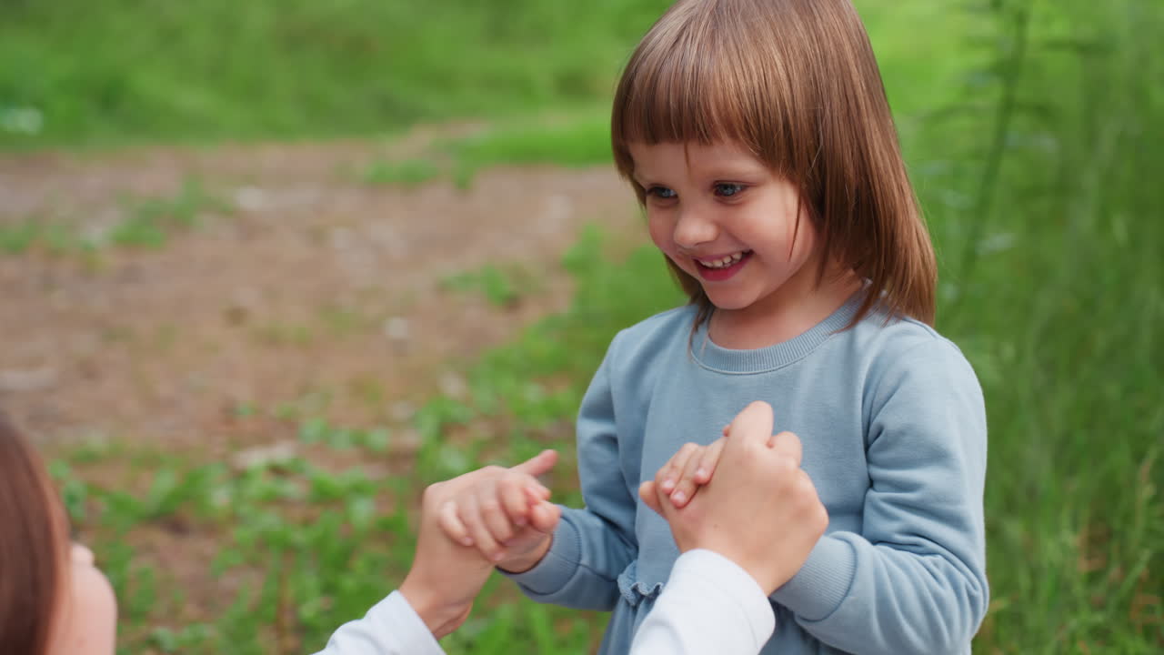 Niña alegre y vivaz sonriendo mientras juega cogida de la mano de su hermana al aire libre en un bosque verde, expresando amor, unión, alegría e inocencia durante un hermoso día soleado lleno de risas