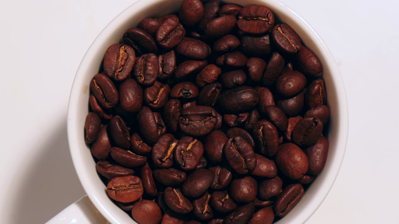 Chicchi di caffè in movimento con tazza bianca.