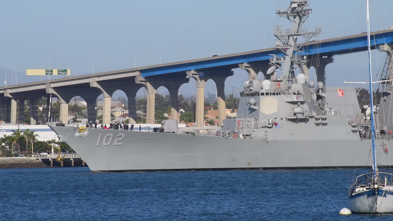 Scenic view of sailboat and seagulls in the blue waters of San Diego Bay with Coronado Bridge and shipyard in the background