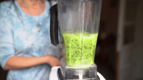 woman making nutritious green vegetable juice blending ingredients