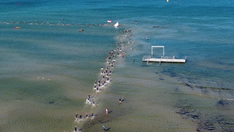 aerial view showing triathlon swimmers running as the shallow blue waters are not deep enough for swim with visible underwater patterns and waves creating a mesmerizing scene