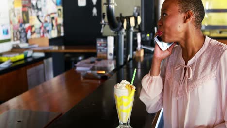 mujer feliz hablando por teléfono móvil mientras toma un batido de leche
