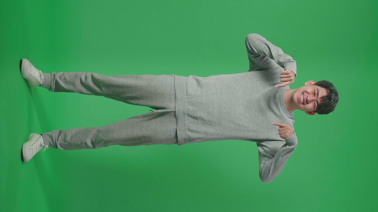 Full Body Of Smiling Asian Man Showing Gesture To Camera While Standing In Front Of Green Screen Background