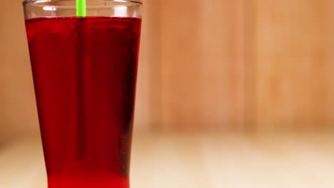 green straw stirring red drink in glass