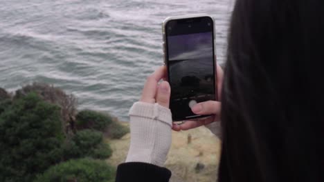 female taking a photo on iphone of the southern ocean along great ocean drive, victoria, australia