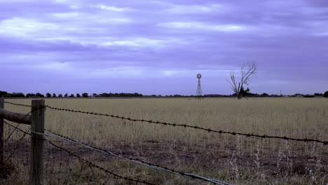 Dürre-Betroffenes-Ackerland-Mit-Einer-Windmühle-Und-Einem-Baum-Im-Hintergrund