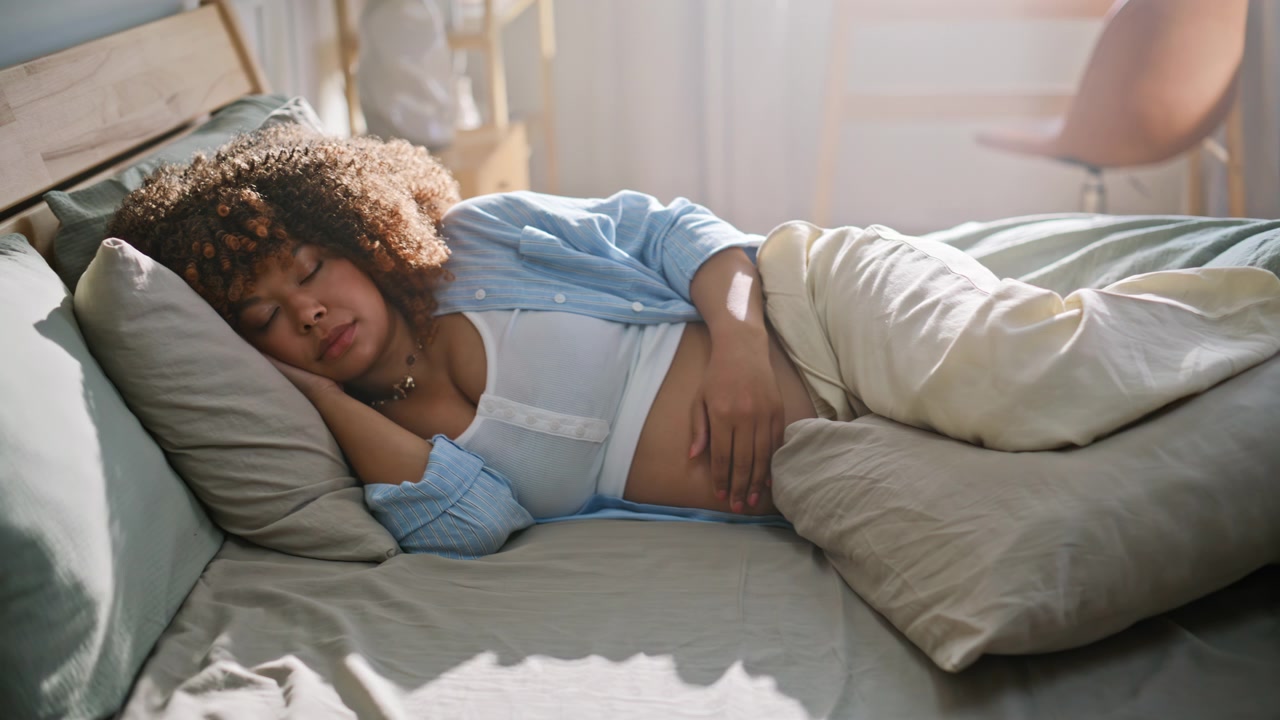 Sleeping future mother holding belly bed. Mom-to-be napping quiet bedroom home.