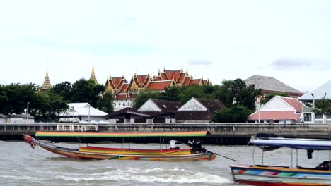 view of beautiful temple on the bank of a busy river with tourist and traditional boats passing by