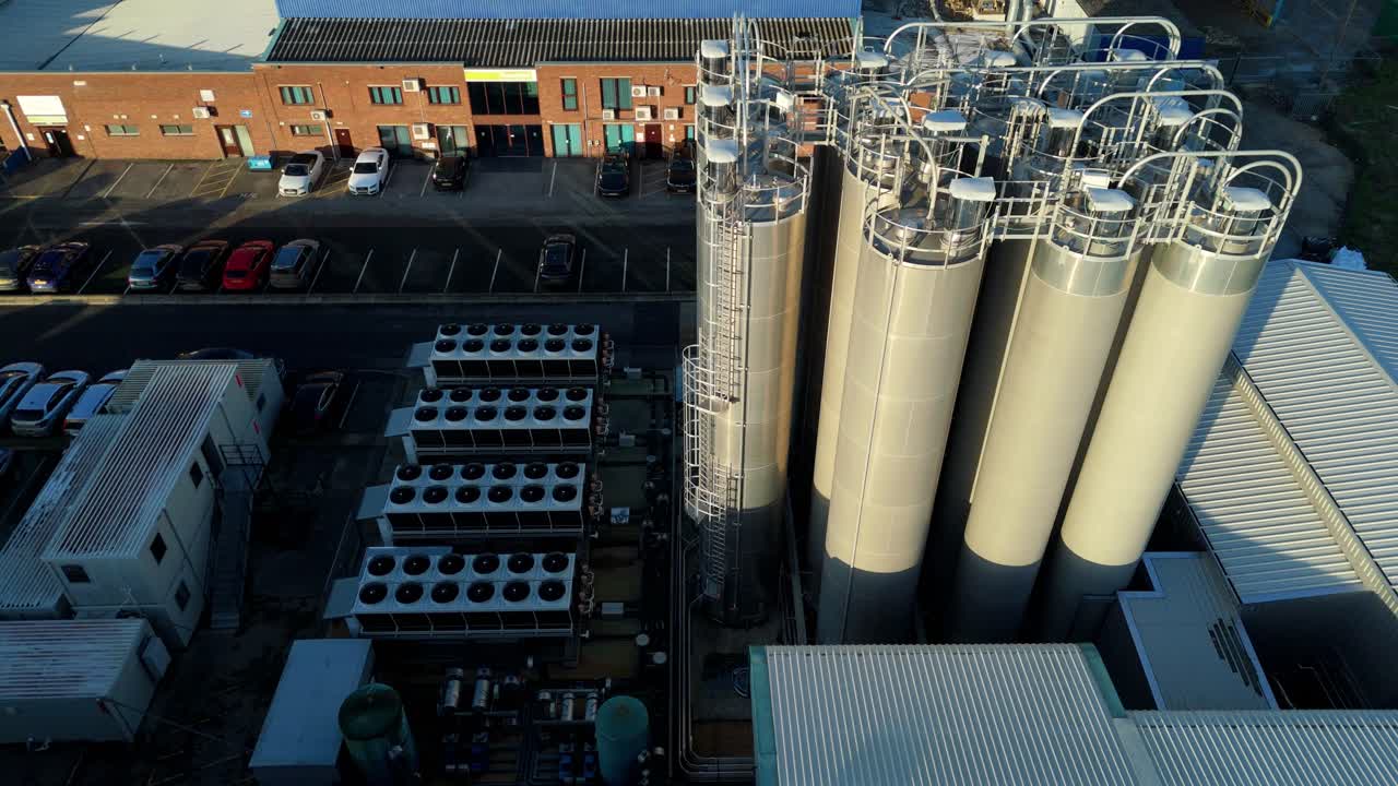 Close-up aerial drone view of industrial storage silos and intricate pipework networks in a major chemical processing facility