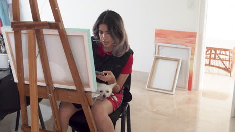 young attractive woman sitting near canvas with white dog on her laps, transition shot to white wall