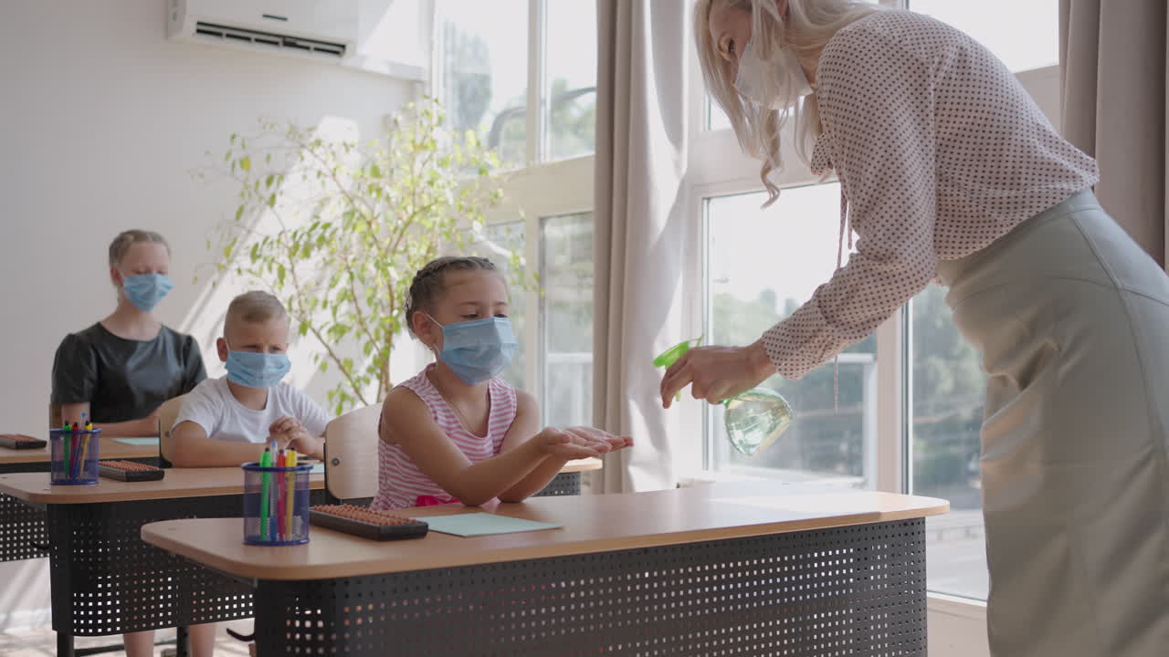 교사는 수업 전에 학교에서 소녀의 손을 살균제로 치료합니다. 코로나바이러스와 학교에서의 전염병. 전염병 모드에서 학교의 작업
