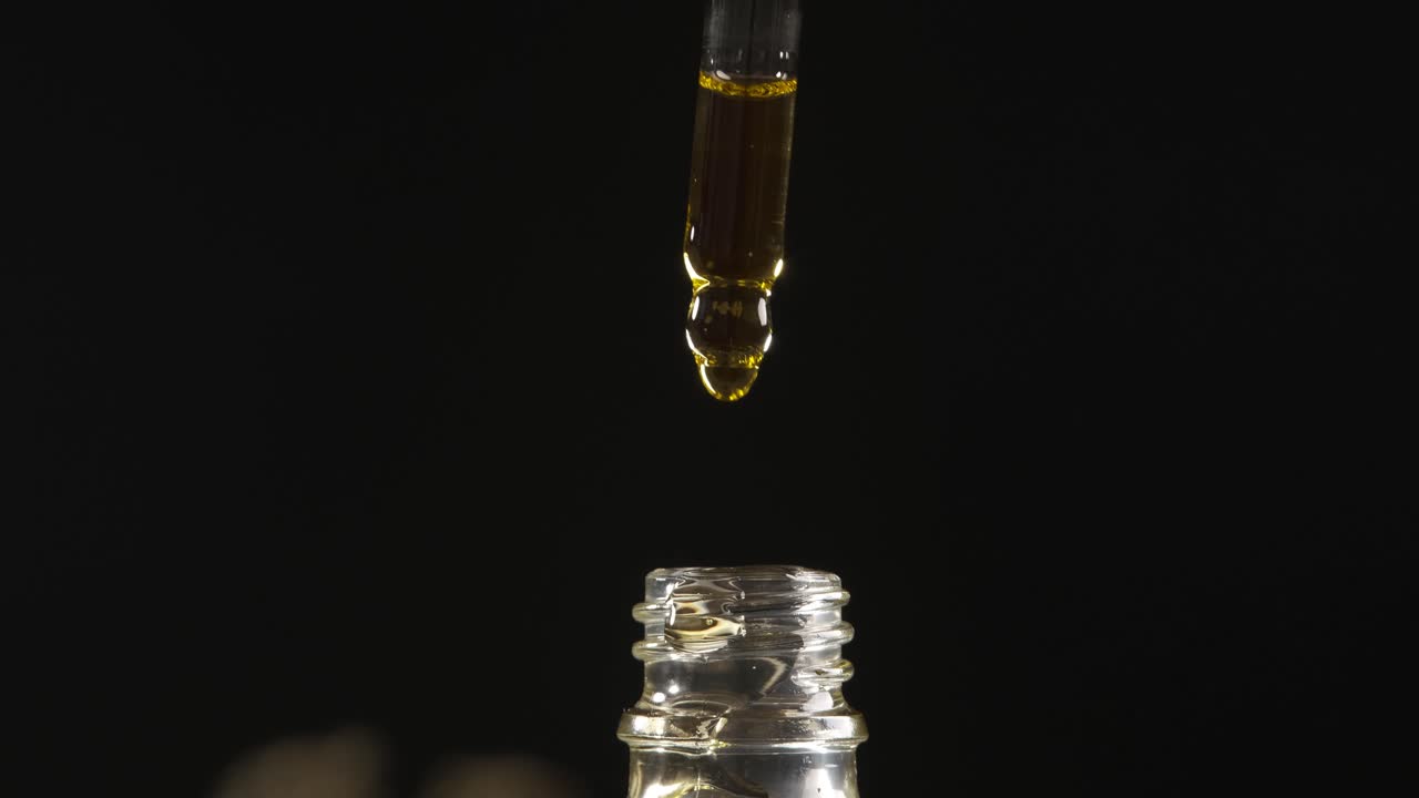Dropper dripping cannabis CBD oil over a dark background.