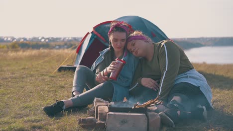 lesbian couple rests at burning bonfire near blue tent