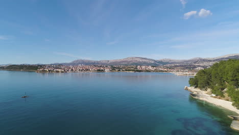 tropical coastline and majestic city of split in distance, aerial ascend shot over seawater