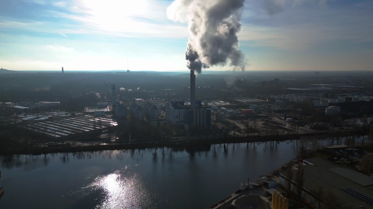 large industrial power plant emitting large amounts of smoke over the city Berlin next to a river on a sunny day. Fantastic aerial view flight wide orbit overview drone
